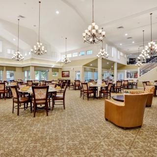 A spacious and elegantly decorated dining area featuring multiple tables and chairs, with chandeliers illuminating the room.