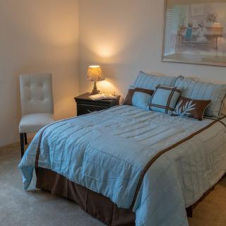 A cozy bedroom with a neatly made bed, a nightstand with a lamp, and a chair in the corner.