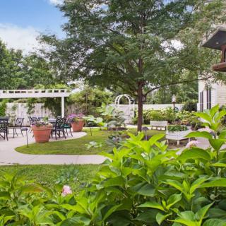 A serene garden with lush greenery, featuring a pergola and outdoor seating.