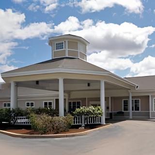 A building with a covered entrance and cupola under a partly cloudy sky.