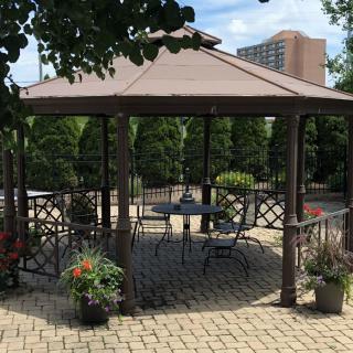 An outdoor gazebo with patio furniture surrounded by greenery in an urban setting.