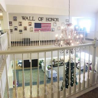 An interior view showcasing a 'Wall of Honor' adorned with photos and an American flag, observed from a balcony with a chandelier overhead.