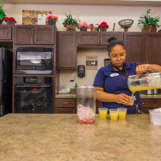 A woman pouring juice into cups on a kitchen countertop.