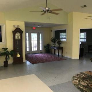 A spacious living room with a grandfather clock, plants, and a ceiling fan.