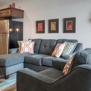 A modern living room featuring a gray sectional sofa adorned with colorful cushions, complemented by framed artwork on the wall.