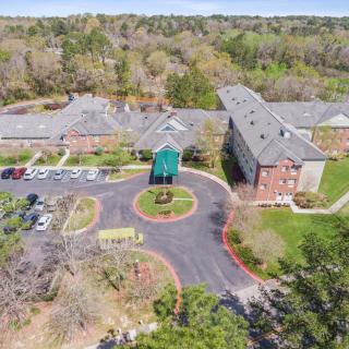 Aerial view of a large building complex with surrounding parking lot and lush greenery.