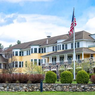 A large building with an American flag in front, surrounded by greenery.