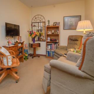 A cozy living room featuring armchairs, a TV, bookshelf, and ambient lighting.