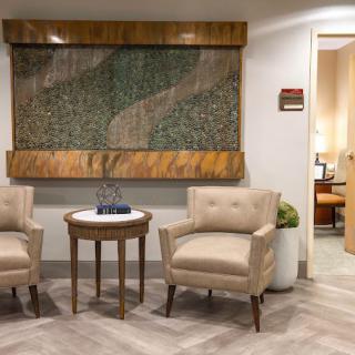 A cozy waiting area with two armchairs and a small table, complemented by wall artwork and a side lamp.
