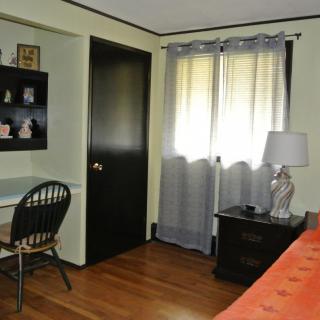A cozy bedroom with a desk and chair, featuring a window with curtains and a lamp on a side table.