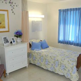 A cozy bedroom featuring a single bed with floral bedding, a white dresser adorned with decorations, and soft blue curtains.