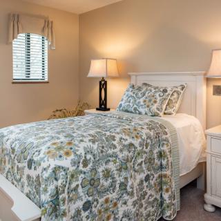 A cozy bedroom features a single bed with a floral quilt, flanked by lamps on nightstands.