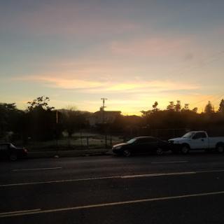 A serene sunset casts a warm glow over the parked cars and landscape.