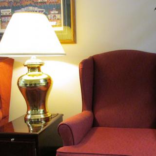 A cozy living room scene featuring a plush red armchair beside a table with a brass lamp.