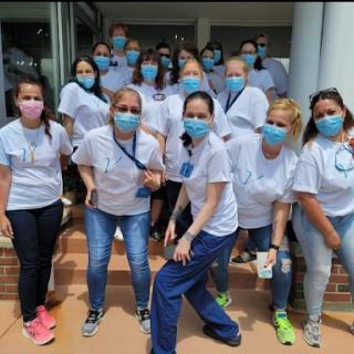 A team of healthcare professionals posing together outdoors, all wearing masks and casual uniforms.