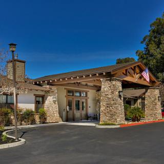 A stone building entrance with an American flag and surrounding greenery under a clear blue sky.