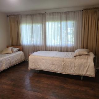 A minimalist bedroom featuring two single beds with wooden flooring and large windows covered by curtains.