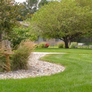 A beautifully landscaped garden featuring green grass, trees, and a curving stone path.