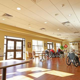 A bright and spacious common area in a nursing home, featuring several wheelchairs and ample natural light.