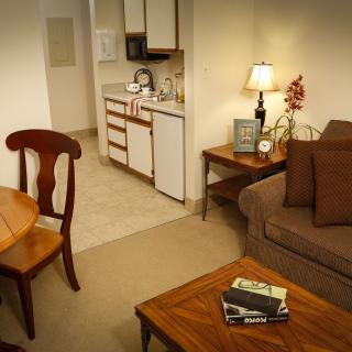 Cozy apartment living area with a small kitchen, featuring warm wooden furniture and soft lighting.