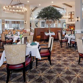 An elegant restaurant interior with neatly arranged dining tables and chairs under a large chandelier.