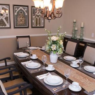 A well-appointed dining room featuring a table set for a meal, adorned with elegant wall art and a floral centerpiece under a chandelier.