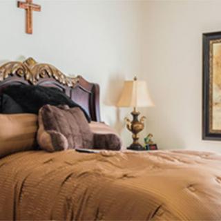 A cozy bedroom with a cross on the wall, plush bedding, and elegant decor.