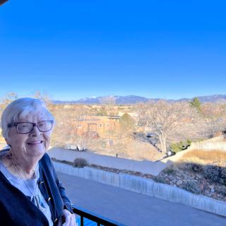 A cheerful senior woman enjoying the scenic view from a balcony.