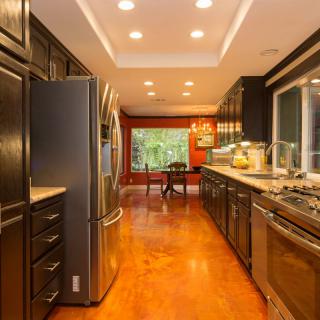 A spacious and modern kitchen with stainless steel appliances, hardwood flooring, and recessed lighting leading to a dining area.