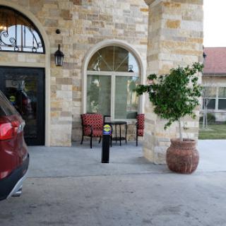 A cozy outdoor seating area in front of a stone building, featuring two chairs and a table beside a potted plant.