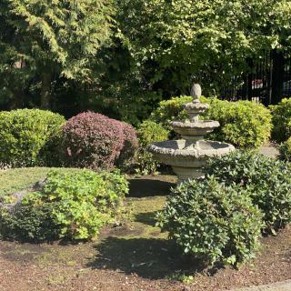 A serene garden scene featuring a decorative stone fountain surrounded by well-manicured bushes and greenery.
