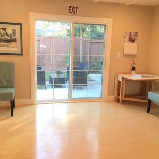 A bright, minimalist room with two chairs, a desk, and a sliding glass door leading to an outdoor area.