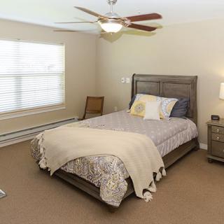 A cozy bedroom with a neatly made bed, ceiling fan, and natural light coming through the window.