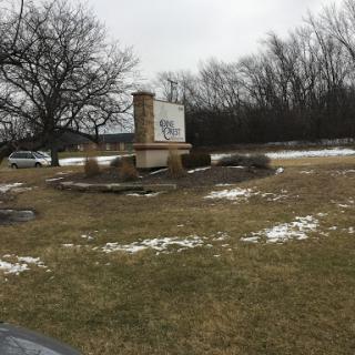 A winter view of a landscape with a sign, bare trees, and patches of snow on the grass.