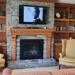 A cozy living room featuring a stone fireplace with a television mounted above, flanked by bookshelves and armchairs.