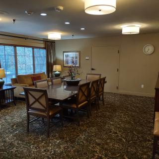 A cozy conference room with a large table surrounded by chairs, featuring warm lighting and a window view.