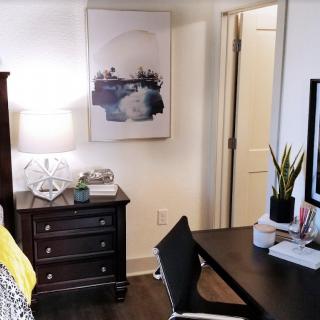 A cozy bedroom setup featuring a desk and chair, with a bedside lamp and wall art adding stylish touches to the decor.