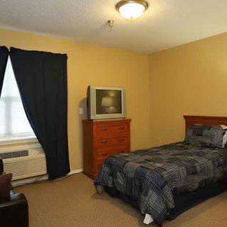 A cozy bedroom with a single bed, a television on a dresser, and dark curtains on the window.