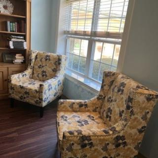 A cozy corner with two patterned chairs by a window and bookshelf.