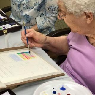 An elderly woman engaged in painting with watercolors at a table.