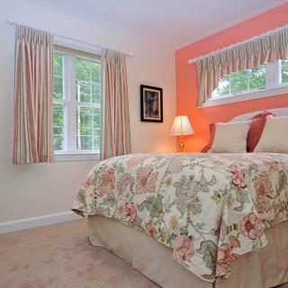 A cozy bedroom with floral bedding, soft lighting, and natural light from a window.