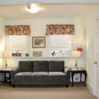 A cozy living room featuring a plush sofa, two side tables with lamps, and windows adorned with floral curtains.