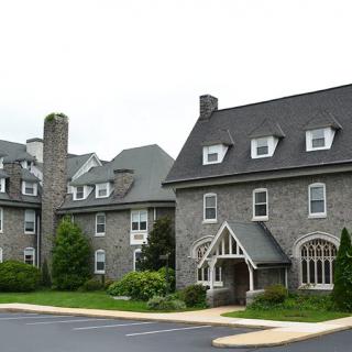 A large stone building with gabled roofs and multiple windows, surrounded by greenery.