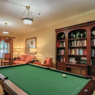 A cozy billiard room featuring a pool table, elegant bookshelves, and comfortable seating.