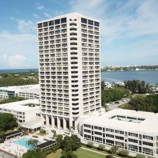 A high-rise building located near a waterfront, surrounded by greenery and additional structures.