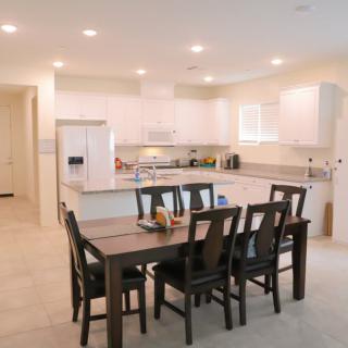 A modern kitchen and dining area with white cabinets and a dark wooden dining table surrounded by chairs.