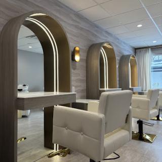 A modern hair salon featuring elegant white chairs and arched mirrors with ambient lighting.