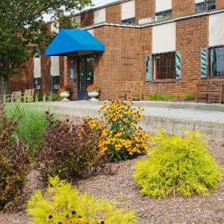 A brick building with a blue awning entrance surrounded by landscaped bushes and flowers.