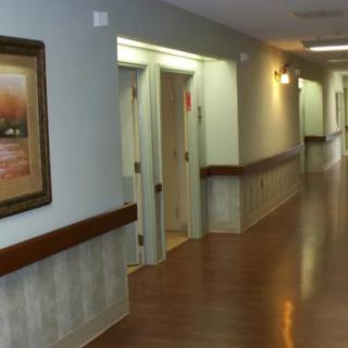 A long, empty hallway in a healthcare facility with wooden flooring and a painting on the wall.