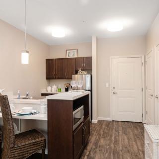 A modern kitchen with a bar counter and wood flooring, featuring dark cabinets and pendant lighting.